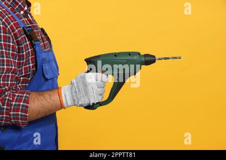 Worker in uniform with power drill on yellow background, closeup Stock Photo