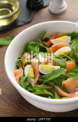 Delicious salad with boiled eggs, salmon and arugula on wooden table, closeup Stock Photo