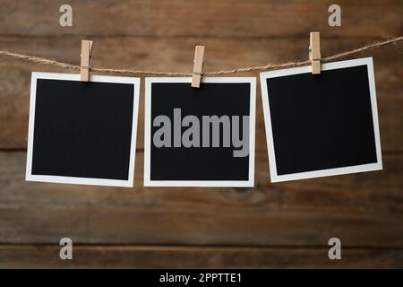 Clothespins with empty instant frames on twine against wooden background. Space for text Stock Photo