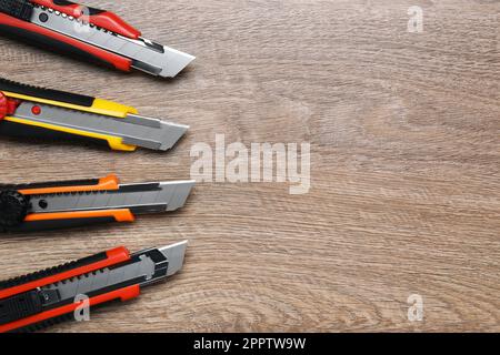 Many different utility knives on wooden table, flat lay. Space for text Stock Photo