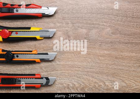 Many different utility knives on wooden table, flat lay. Space for text Stock Photo