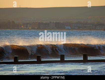 Portobello, Edinburgh, Scotland, UK. 25th April 2023. A nippy sunrise 2 degrees at dawn by the Firth of Forth with the sun slowly rising over the dark clouds on the horizon. Pictured: A larger swell than is usual at Port Beach. Credit: Arch White/alamy live news. Stock Photo