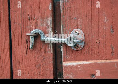 hook lock latched to bent nail on a red wood door Stock Photo