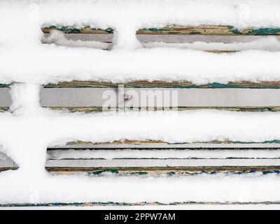 top view of snow-covered planks of old wooden bench close-up in city park on overcast winter day Stock Photo