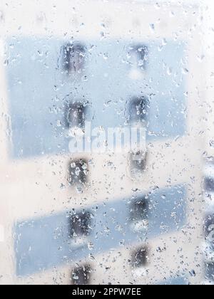 rain drops on surface of window glass in city apartment and view of urban house on background Stock Photo