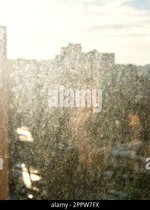 dirty surface of window glass in city apartment lit by sunset sun and view of street on background Stock Photo