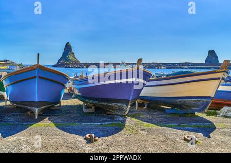 Aci Trezza, Italy, the stacks of the Cyclops marine reserve seen from the harbor with colorful fishermen boat in the foreground Stock Photo