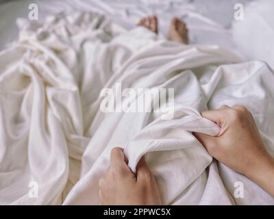A cropped view of two hands holding on a rumpled bedspread Stock Photo