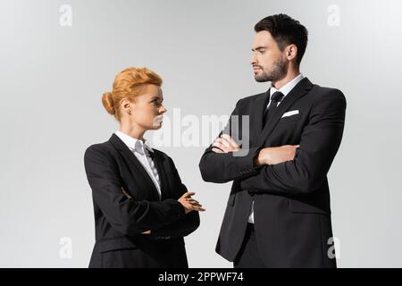 confident businessman looking at serious redhead businesswoman isolated on grey,stock image Stock Photo