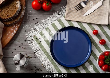 An empty blue plate as serving on the table. Table setting with vegetables and bread on a grey background. Stock Photo