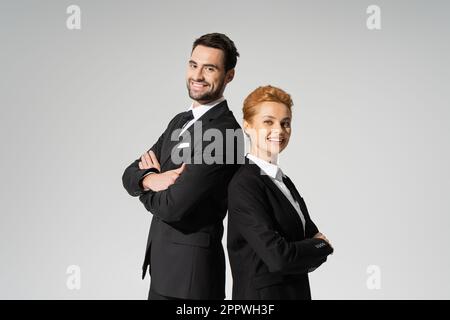 successful corporate managers in black suits standing back to back and smiling at camera isolated on grey,stock image Stock Photo