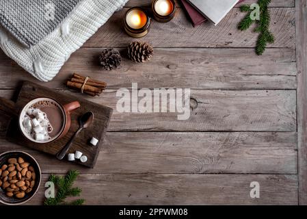Hot coffee drink, almonds, cosy knitted sweater on wooden background with candles and pine cones, copy space. Hygge and home comfort concept. Seasonal Stock Photo