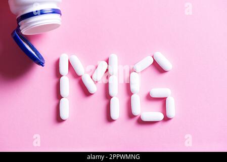 Mineral pill capsule Magnesium. White vitamin pills forming shape to Mg sign and plastic bottle on pink background, copy space, top view. Stock Photo