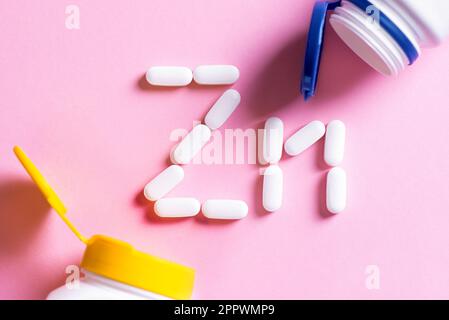 Mineral pill capsule Zinc. White pills forming shape to Zn sign and plastic bottles on pink background close up. Stock Photo