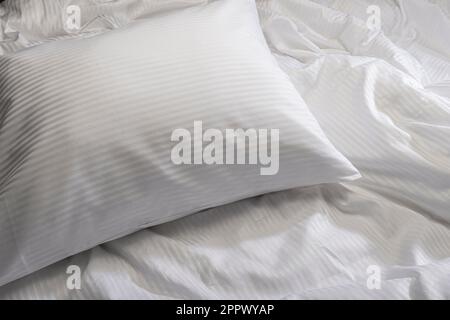White pillow on bed with wrinkled sheets Stock Photo