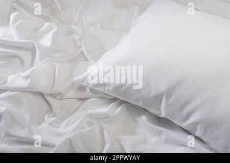 White pillow on bed with wrinkled sheets Stock Photo