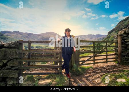 Archive photo of a young caucasian female walking through a wooden kissing gate in the Cumbrian countryside. UK Stock Photo