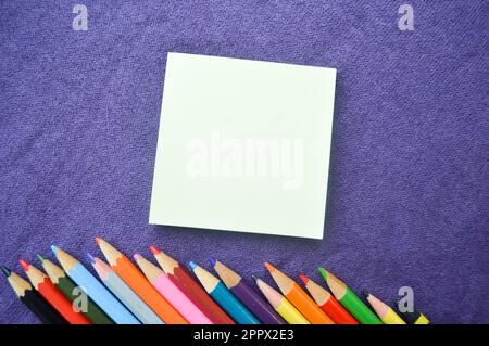 Multicolored, bright, colorful pencils are located at the bottom at an angle and a notebook for your text on a violet background. Stock Photo