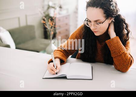 Young woman multitasking: writing in journal and studying for success. Close-up view of woman writing in copybook for studying or making checklist Stock Photo