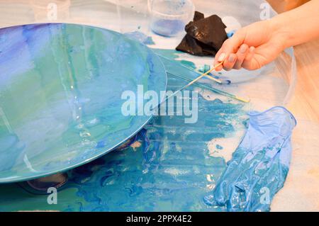 The process of creating a home-made trendy abstract modern pattern painted with a brush of acrylic blue multi-colored resin on a round wooden board. Stock Photo