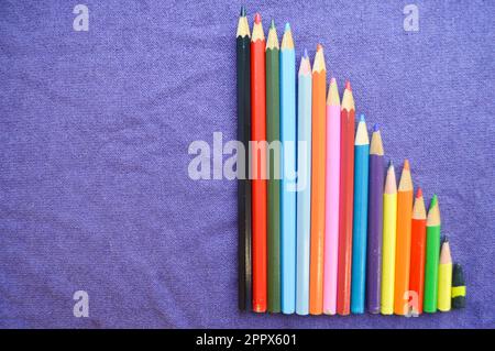 A descending chart of colorful, bright, variegated drawing pencils and space for text on a purple background. Stock Photo