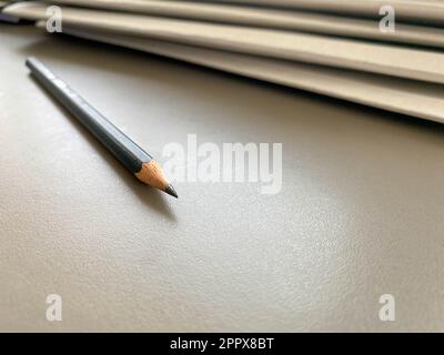 A simple black pencil lies sharply sharpened next to folders with sheets of paper and documents on the working business desk in the office. Stationery Stock Photo