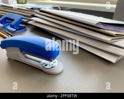 A large blue stapler for stapling paper lies next to the folders of documents on the working business desk in the office. Stationery. Stock Photo