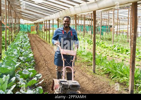 Portrait of smiling male farmer plowing soil using tractor cultivator in greenhouse Stock Photo