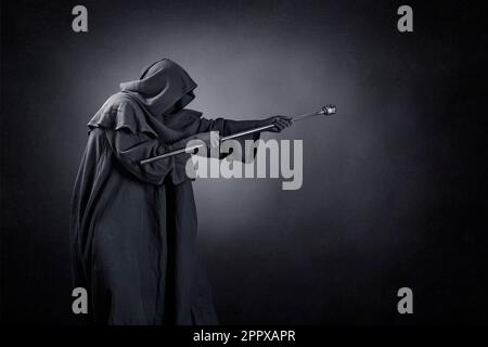 Wizard with hooded cape and magic staff over dark misty background Stock Photo