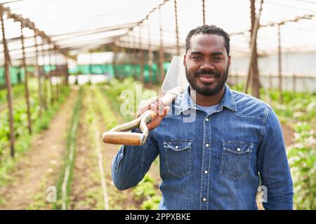 Portrait of smiling young male farmer with shovel in organic farm on sunny day Stock Photo
