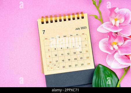 July 2023 calendar desk and pink orchid on pink background. Stock Photo