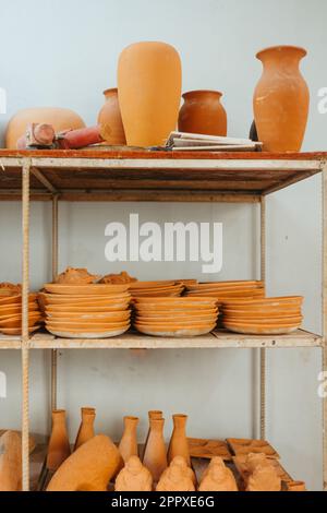 Collection of various handmade clay vases and different plates arranged on shelves against white background in workshop Stock Photo