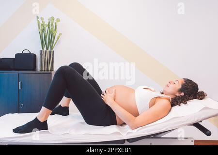 Side view of young female pregnant lying on soft bed of massage table and relaxing after session in osteopathy clinic Stock Photo
