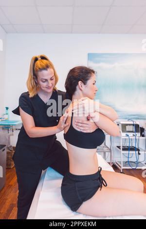 Confident female therapist in black uniform massaging back of patient during rehabilitation session on medical table in modern salon Stock Photo