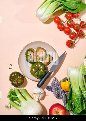 Green tomatoes with other vegetables as bok choy in bright sunlight flat lay plate with knife with copy space on beige background Stock Photo