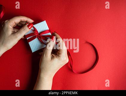 Anonymous woman holds the white box with red ribbon on red background Stock Photo