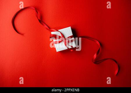 White gift box with red ribbon on bright red background Stock Photo