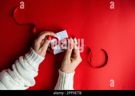 Anonymous woman holds the white box with red ribbon on red background Stock Photo