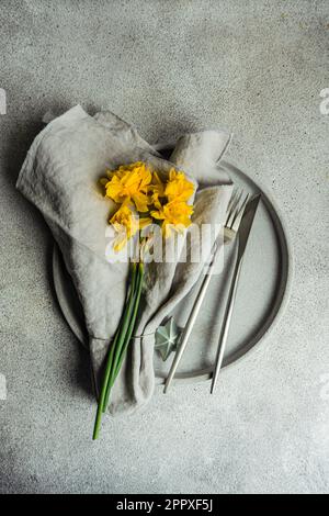 Top view of monochrome concrete table setting with daffodil flowers on the grey cement background Stock Photo