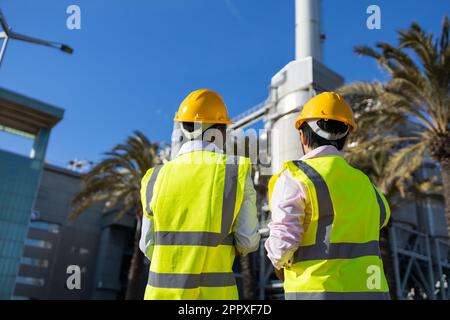 Low angle back view of anonymous engineers in protective helmet and yellow uniform standing together on construction site Stock Photo