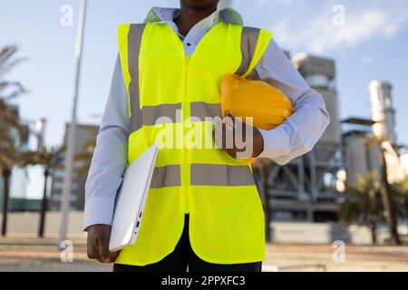 crop anonymous African American female engineer in uniform and helmet and laptop standing on construction site during work Stock Photo