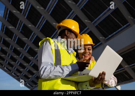 Low angle of young happy female builders in hardhat and uniform using laptop while working together and discussing project on construction site Stock Photo