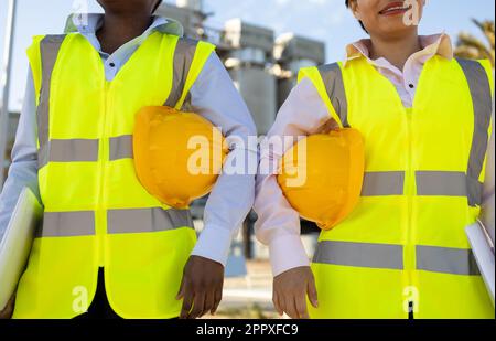 Anonymous african american female engineers in uniforms and helmets standing together on construction site during work Stock Photo