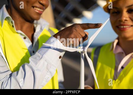Crop builders in uniforms and helmets using wind turbine while working together on construction site Stock Photo