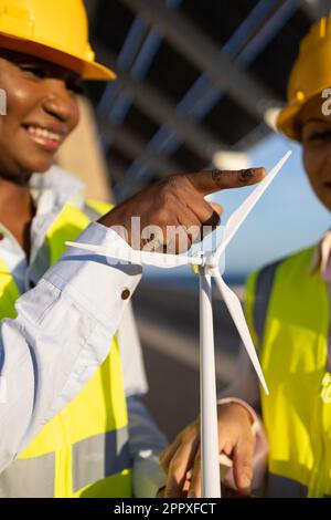 Crop builders in uniforms and helmets using wind turbine while working together on construction site Stock Photo