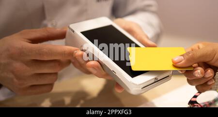 High angle of crop anonymous hand of woman making contactless payment with credit card in optical store while buying new eyewear Stock Photo