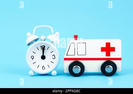 Ambulance toy wooden block and alarm clock on blue background. Emergency healthcare medical concept. Stock Photo