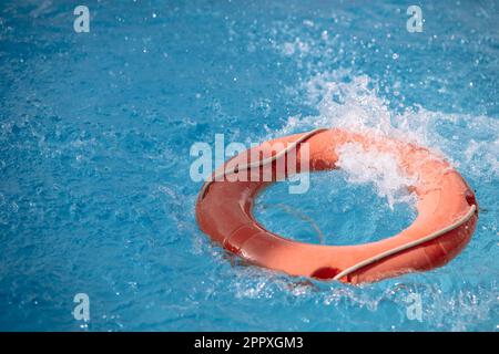 Bright inflatable tube ring floating on blue water surface with splashes in swimming pool during daytime Stock Photo