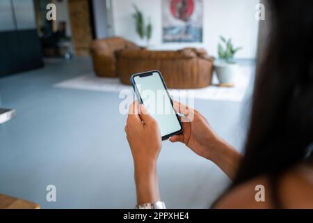 From above cropped unrecognizable young female in casual clothes sitting on sofa and browsing smartphone while resting in cozy living room at home and Stock Photo