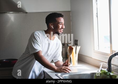 Side views of positive young ethnic African American male in casual outfit smiling and singing in wooden spatula while listening to music in true wire Stock Photo